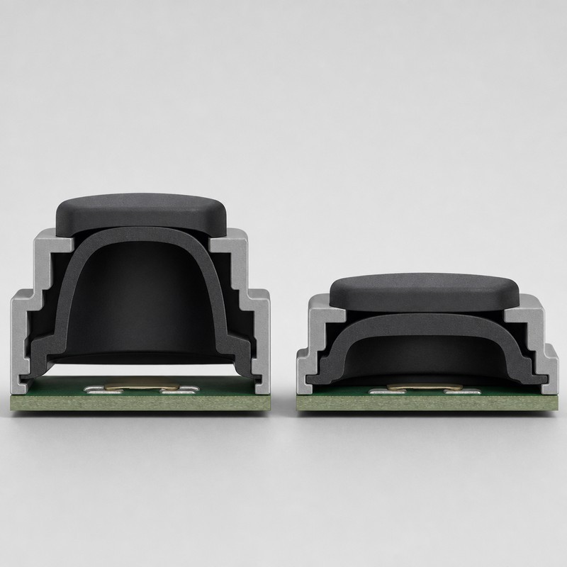 Two silicone keypad buttons side by side inside a grey housing, one with a tall rubber dome and one with a compressed short dome above the circuit board