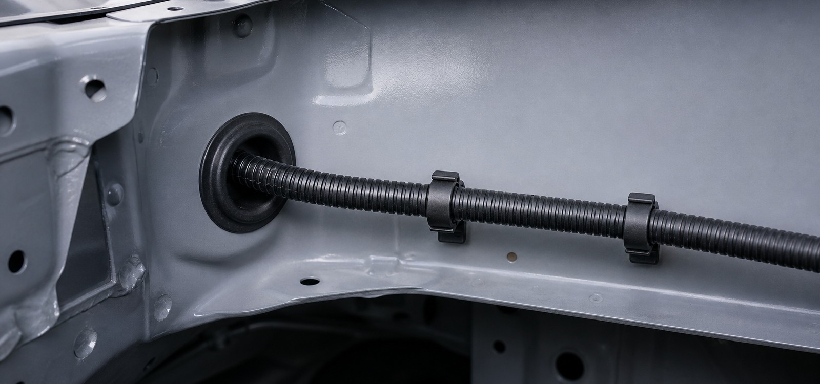 Automotive wire harness with corrugated conduit routed along a painted steel body panel through a rubber grommet in the firewall