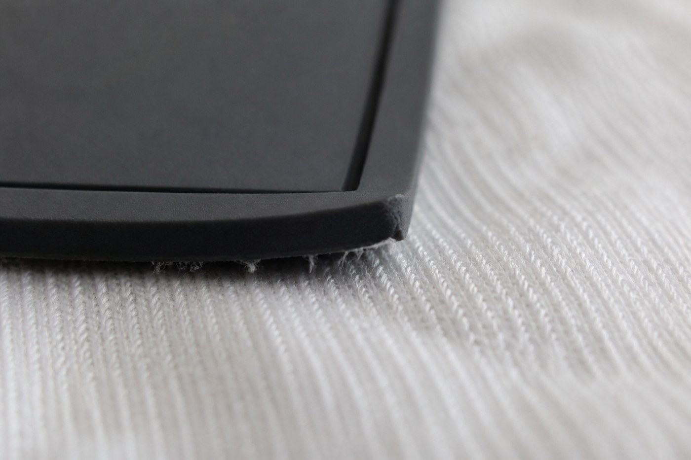 Close-up of a silicone patch corner lifting away from white cotton fabric after washing