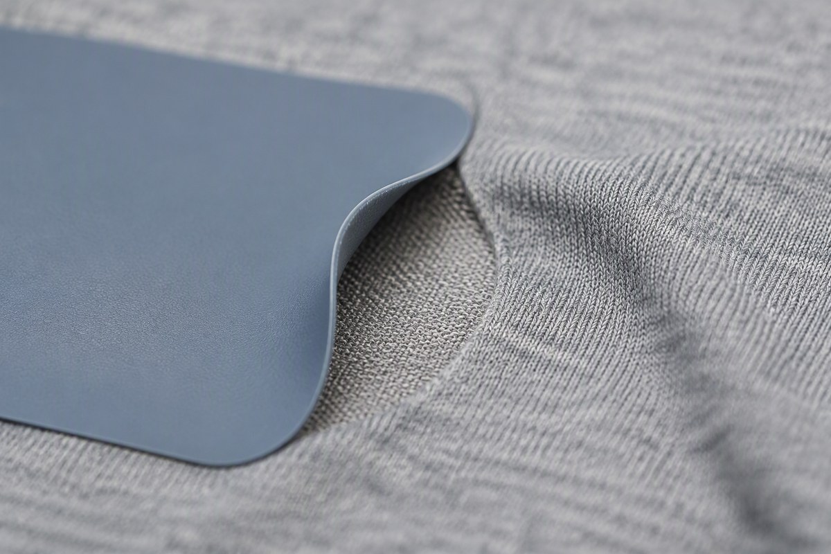 Edge of a silicone heat transfer label peeling from polyester knit fabric after laundering, showing the separation interface on polyester