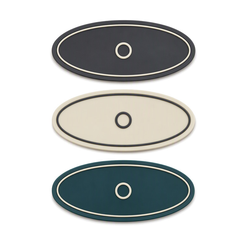 Oval silicone labels with a fine raised pinstripe frame and centred ring motif in charcoal, cream and teal