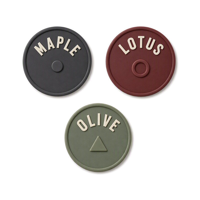 Round moulded silicone labels with raised arced wordmarks in charcoal, burgundy and olive above a small centred symbol