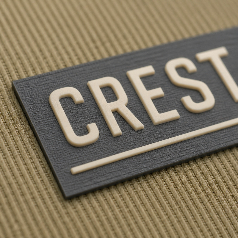 Macro view of a compact molded silicone clothing label with raised cream lettering and a rule on charcoal twill cap fabric