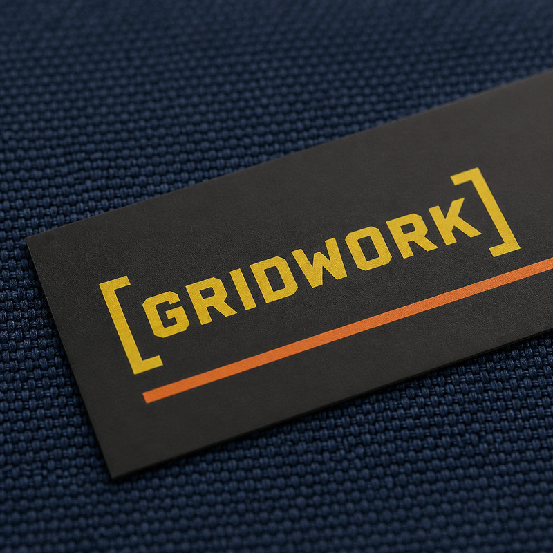 Screen-printed flat silicone clothing label with yellow lettering and an orange rule on dark woven fabric, compared with molded silicone detail at small logo sizes