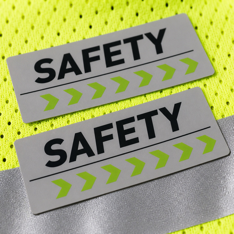 Flat screen-printed silicone labels with black lettering and green chevrons on high-visibility mesh, contrasted with molded 3D silicone relief