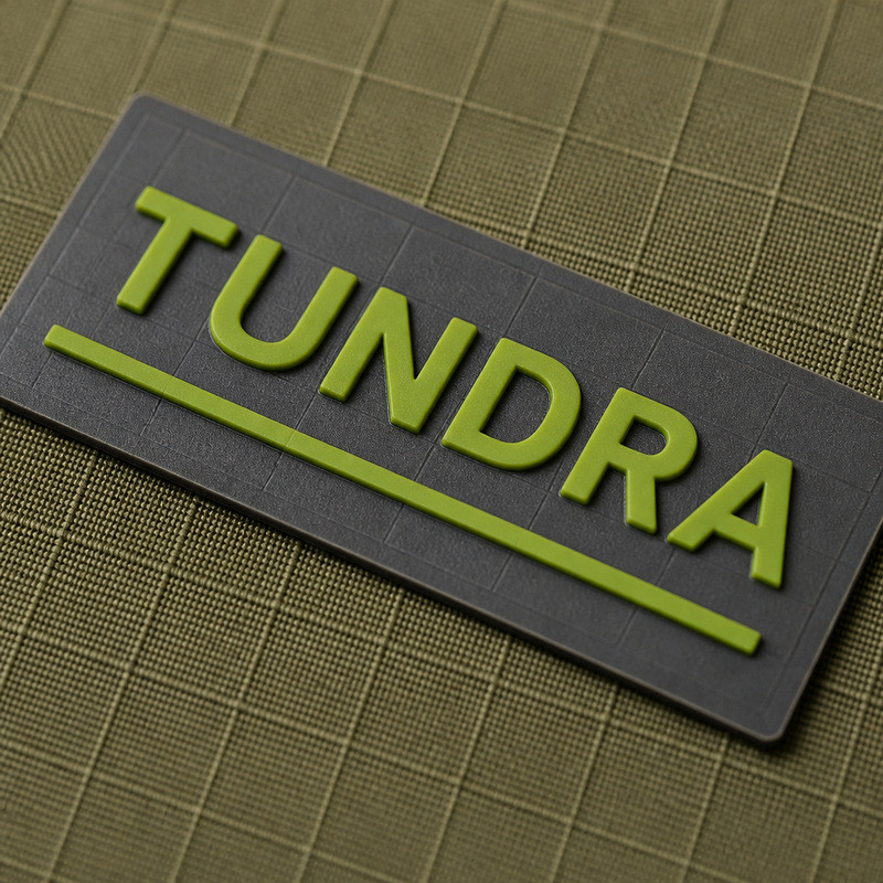 Molded 3D silicone patch with raised lime lettering and a rule on olive ripstop fabric, showing patch edge behavior on grid-structured textile