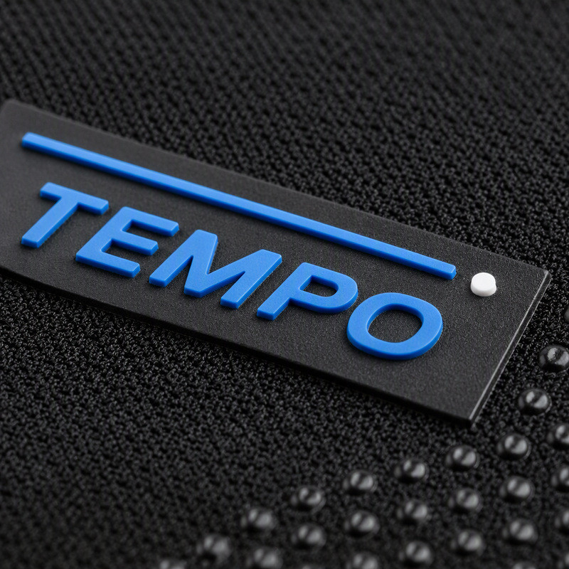 Small molded silicone patch with raised blue lettering and a single white dot on black compression knit fabric