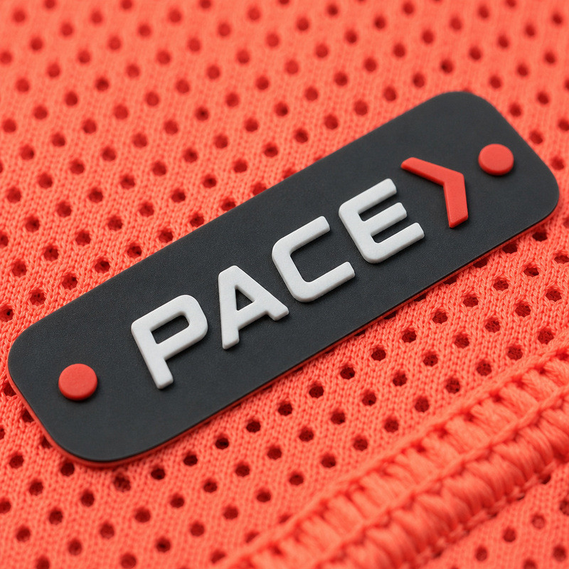 Small dark molded silicone patch with raised white lettering and a red chevron on red honeycomb mesh sportswear fabric