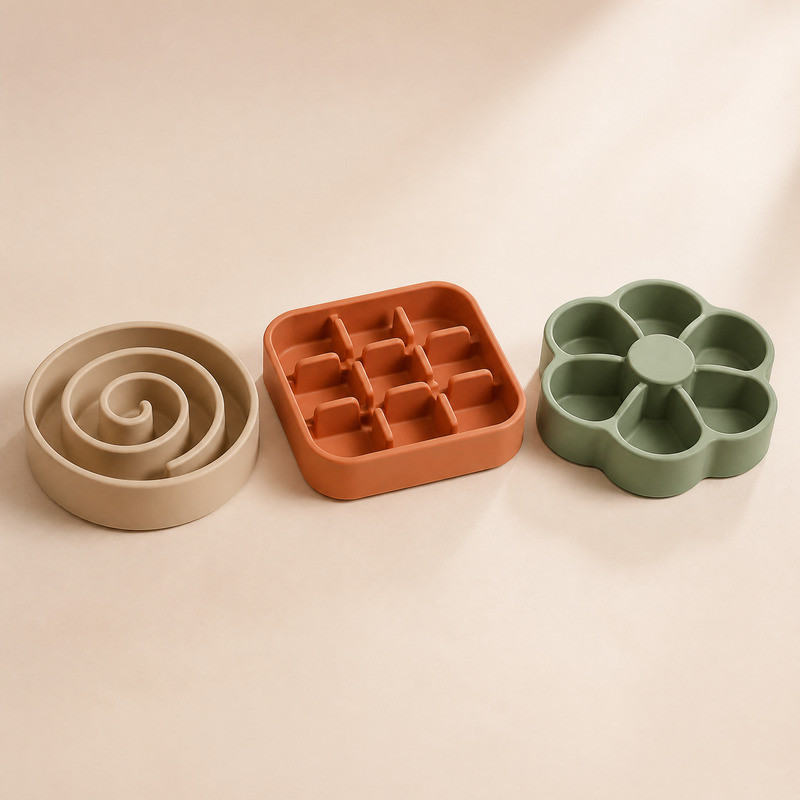 Four silicone slow feeder bowls with radial maze patterns in green, terracotta, beige and charcoal