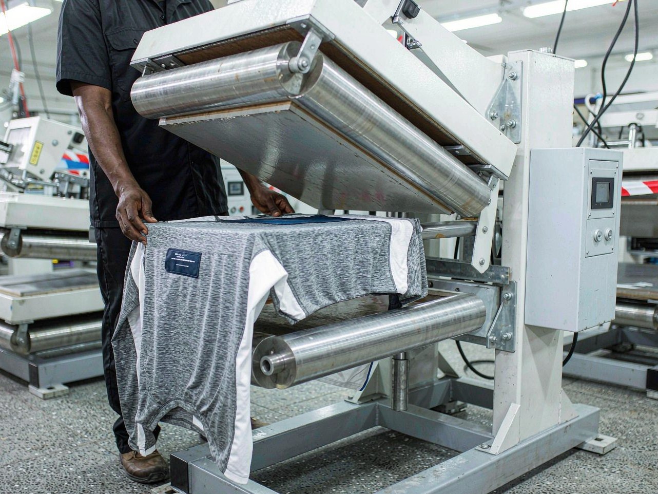 Technician pressing a raised silicone heat transfer label onto black performance sportswear with a pneumatic heat press