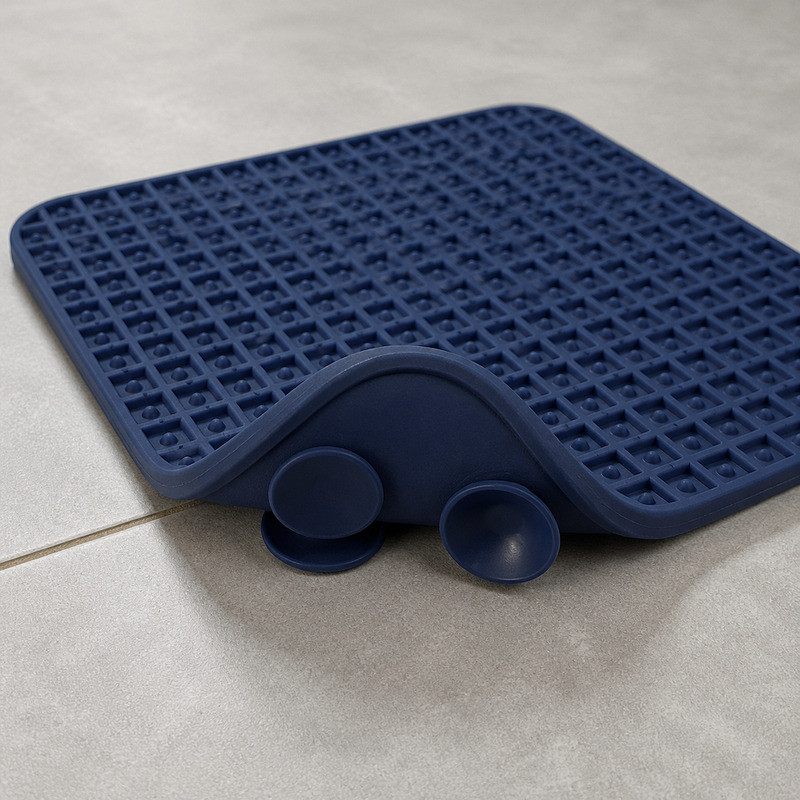 Navy blue silicone lick mat turned over on a tiled floor, showing the moulded suction cups on the underside