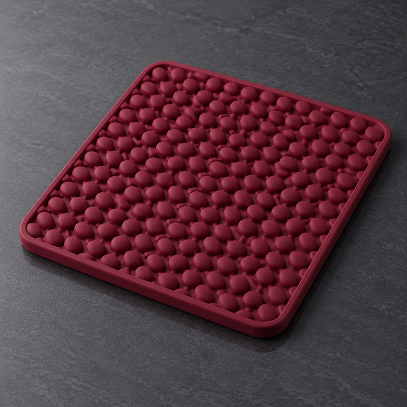 Burgundy silicone lick mat with a raised pebble texture, photographed at an angle on a dark surface