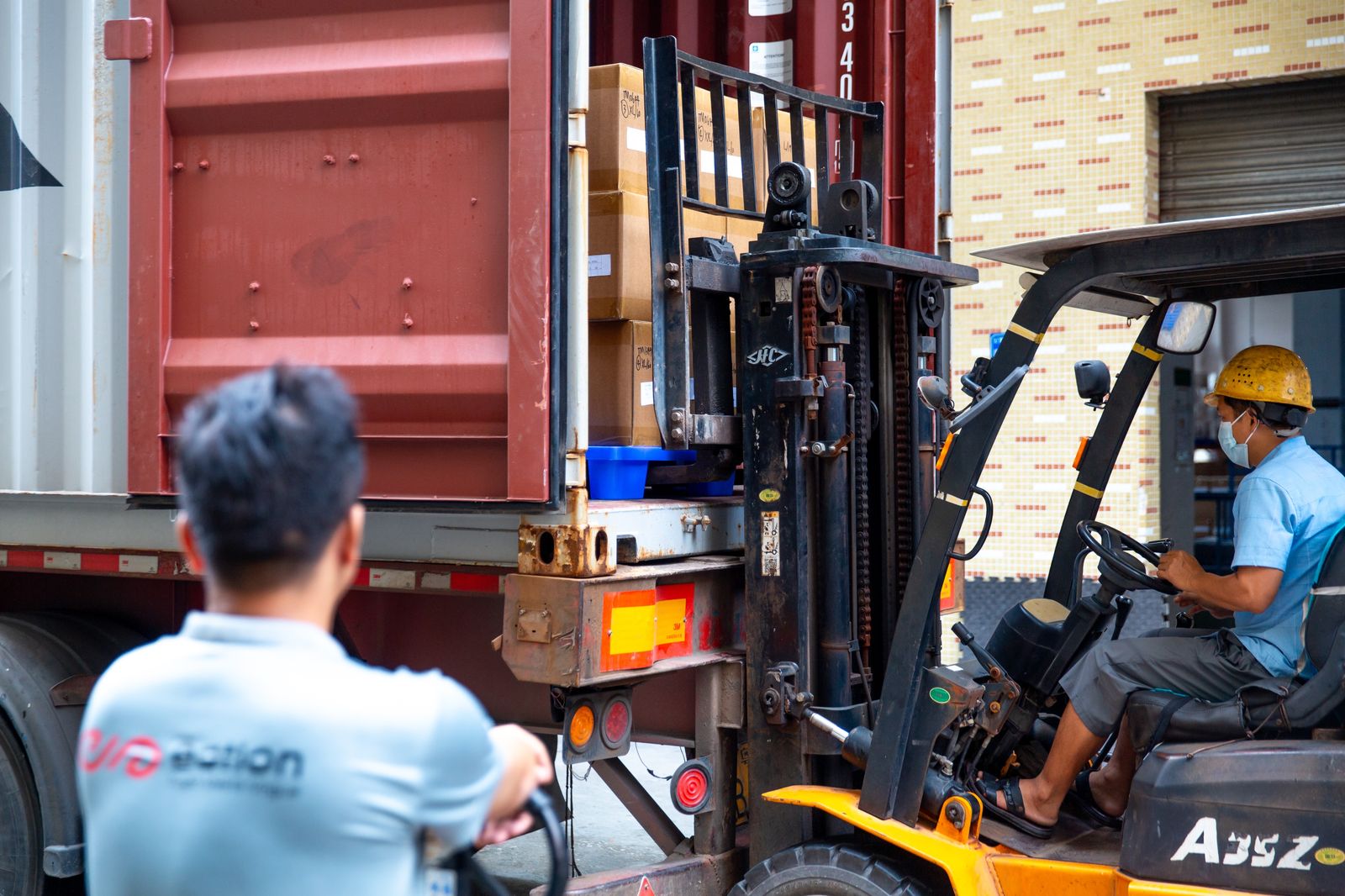 Forklift operator loading cartons into a shipping container at the factory loading dock