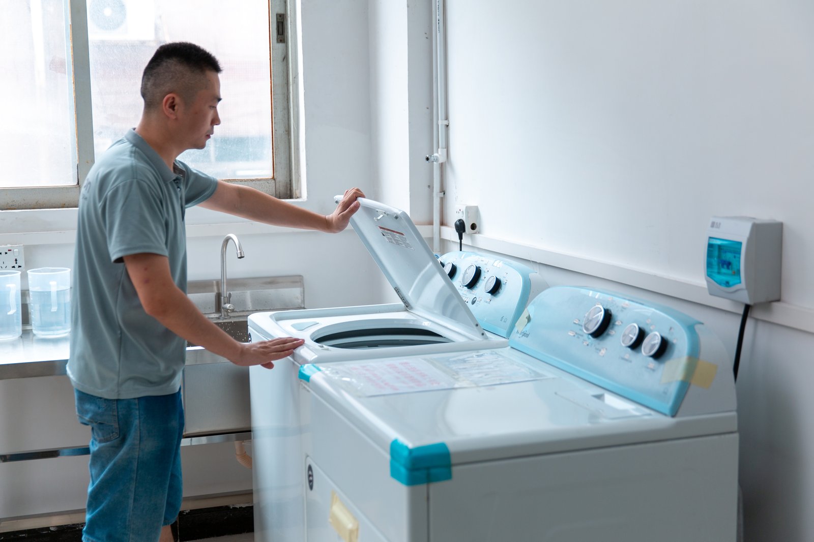 Wash/shrinkage test station at a sportswear factory: washing machines and a technician checking garments — where bulk lots are tested for shrinkage and pilling before shipment