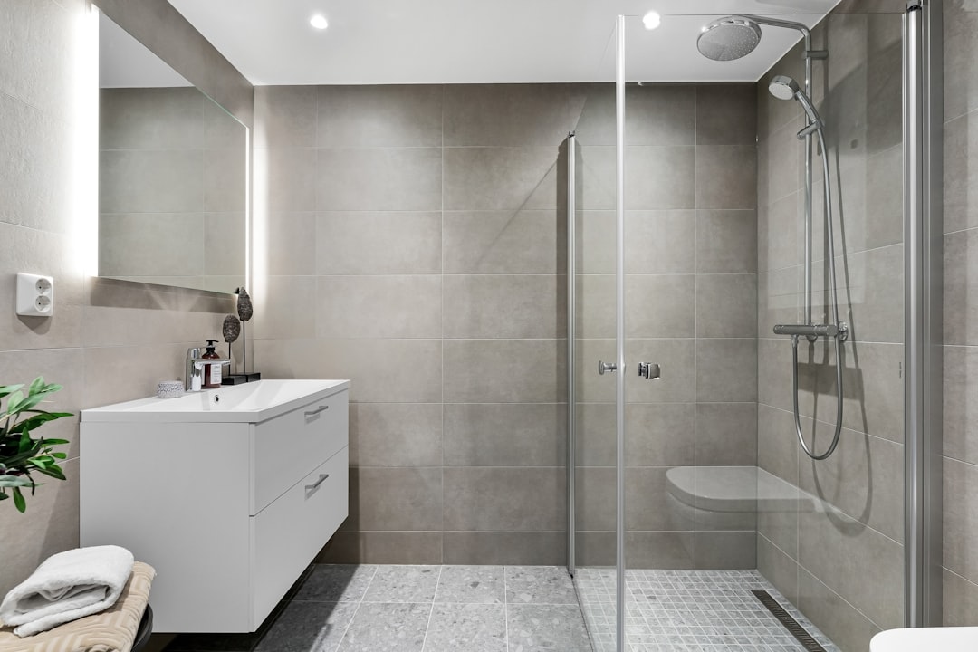 A modern bathroom showcasing sleek silver aluminium tile trim along the edges of grey wall tiles.