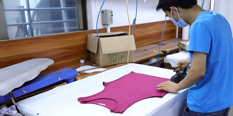 Worker ironing a pink activewear garment at an Ohsure production workstation