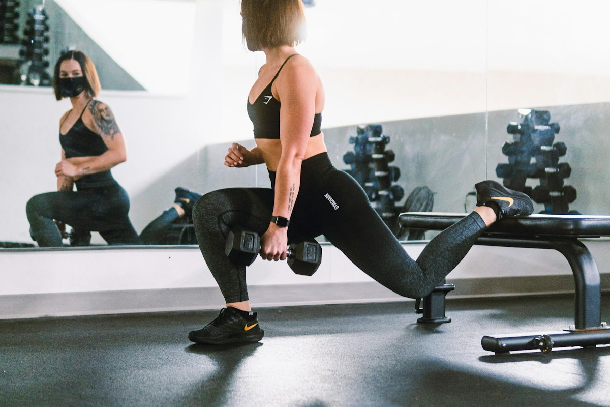 Woman in leggings performing a rear-foot-elevated split squat with dumbbells