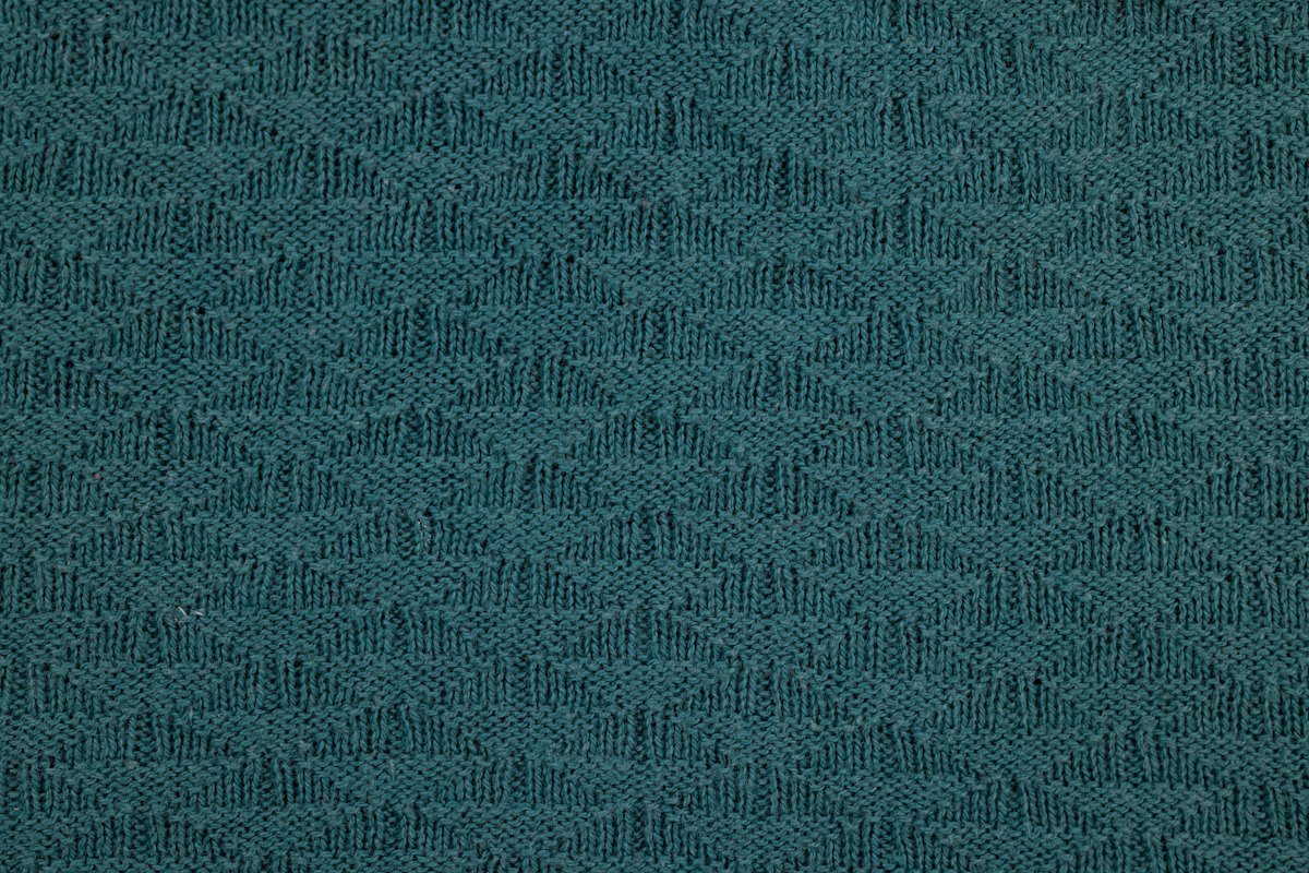 Close-up of teal knitted fabric showing yarn loops and surface texture