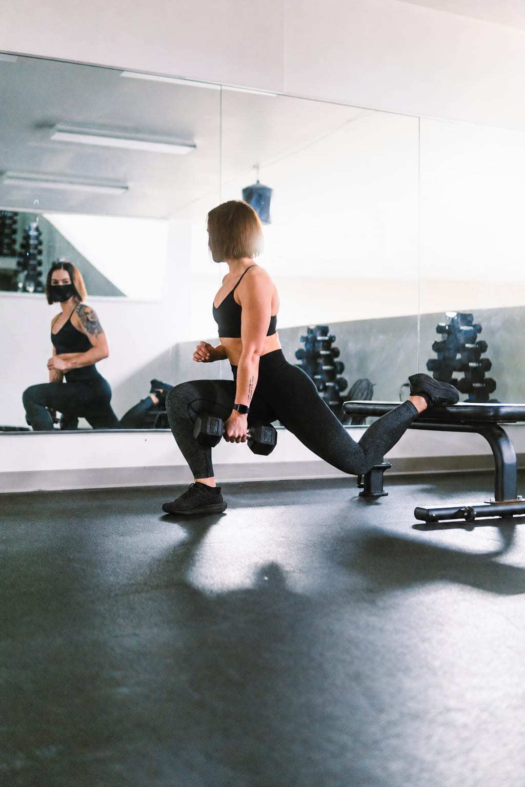 Woman wearing a black sports bra and fitted leggings during a dumbbell split squat