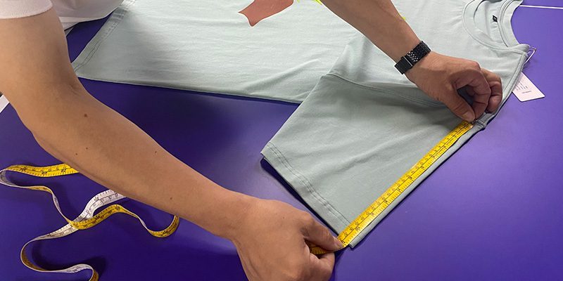 A person measures a garment on a worktable in an image from Ohsure’s manufacturing page