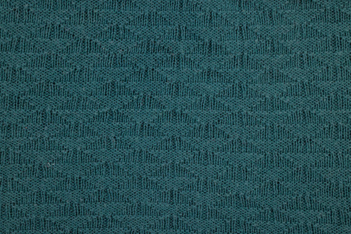 Close-up of teal knitted textile showing loops and a raised surface pattern