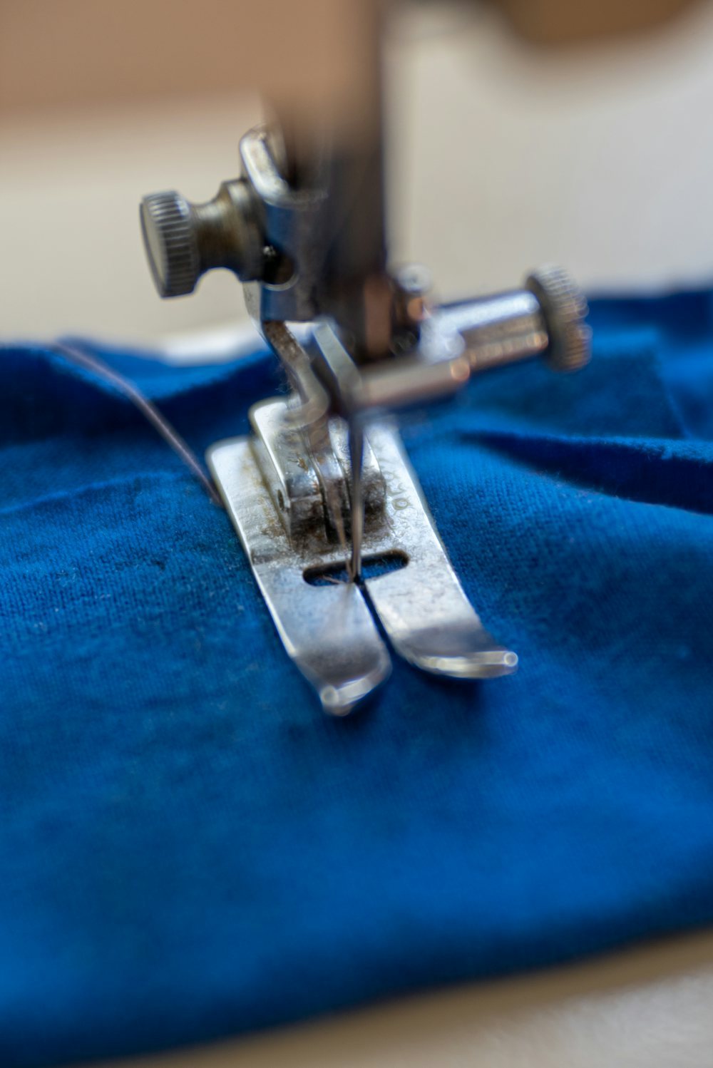 Sewing machine needle and presser foot over blue fabric