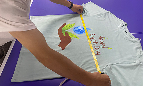 A T-shirt laid flat on a purple table and measured with a tape