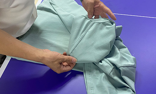 Hands checking the seam area of a garment on an inspection table