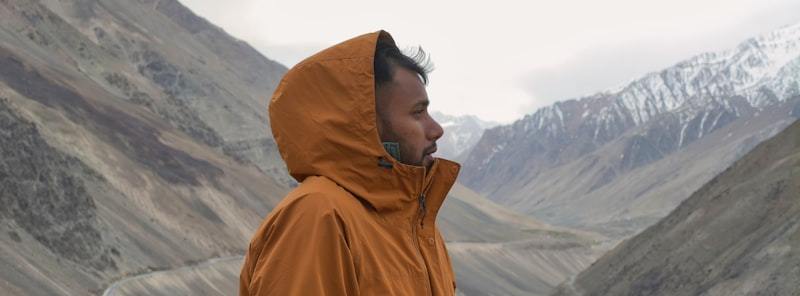 Hiker in orange hooded jacket overlooking snowy mountain landscape