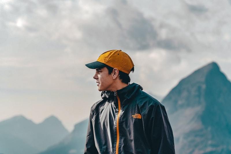 Man in blue jacket and yellow cap standing on mountain