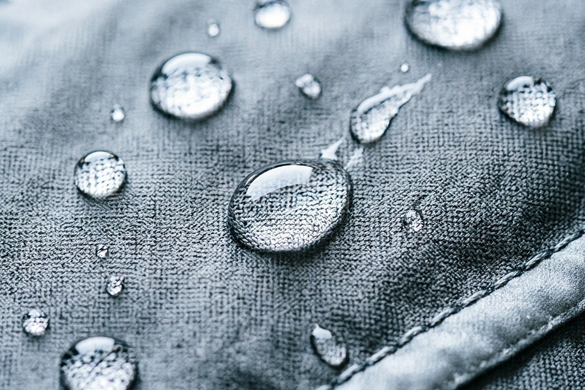 Close-up of water beading and rolling off a treated grey technical outdoor jacket fabric