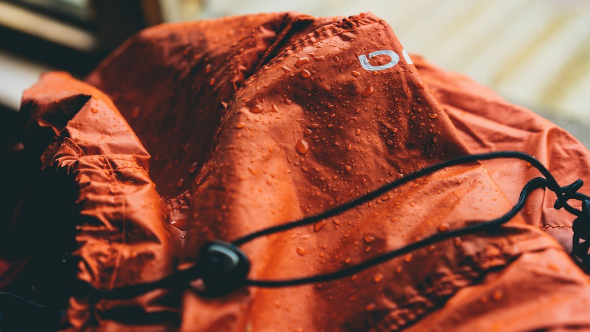 Waterproof zipper and storm flap detail on an orange shell jacket