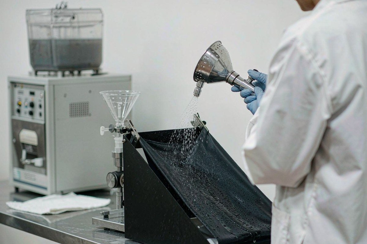 Textile laboratory technician running a spray water-repellency rating test on a fabric swatch