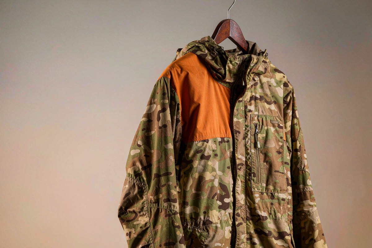 Close-up of a camouflage hunting jacket with a high-visibility blaze orange panel and a radio pocket