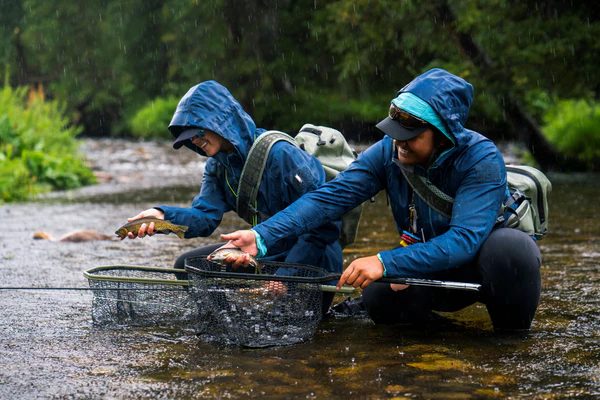 Anglers in waterproof fishing apparel wading a river in rain