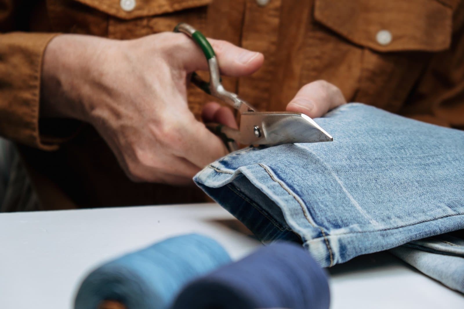 tailor-in-sewing-studio-works-with-jeans-cuts-off-the-extra-length-of-jeans-with-scissors-close-up