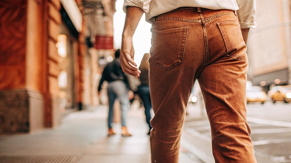 A person's legs walking in well-worn Levi's jeans on a city street.