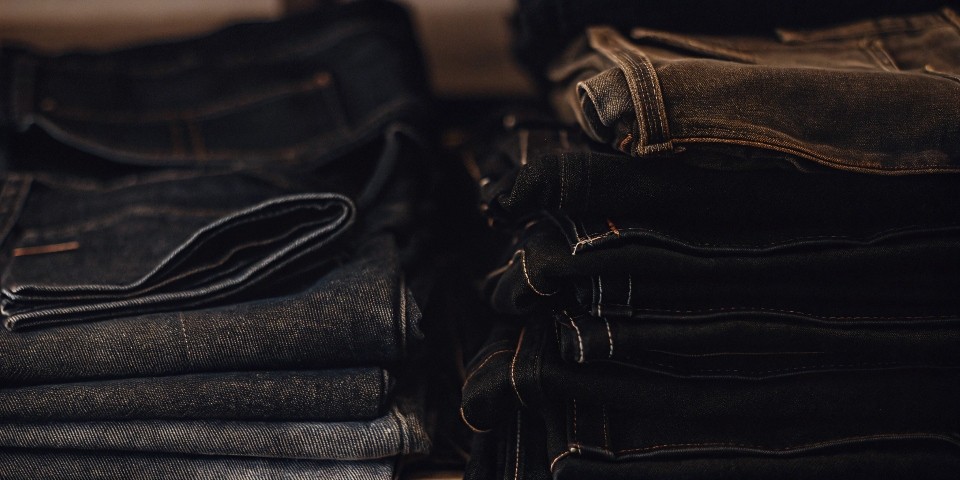 A pile of folded jeans, some new and dark, some old and faded.