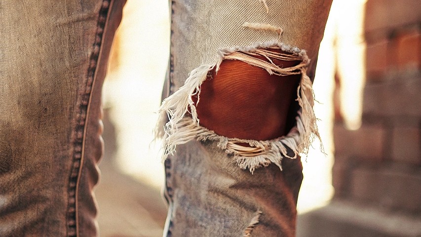 A close-up of a torn knee on a pair of jeans, showing clear wear and tear.
