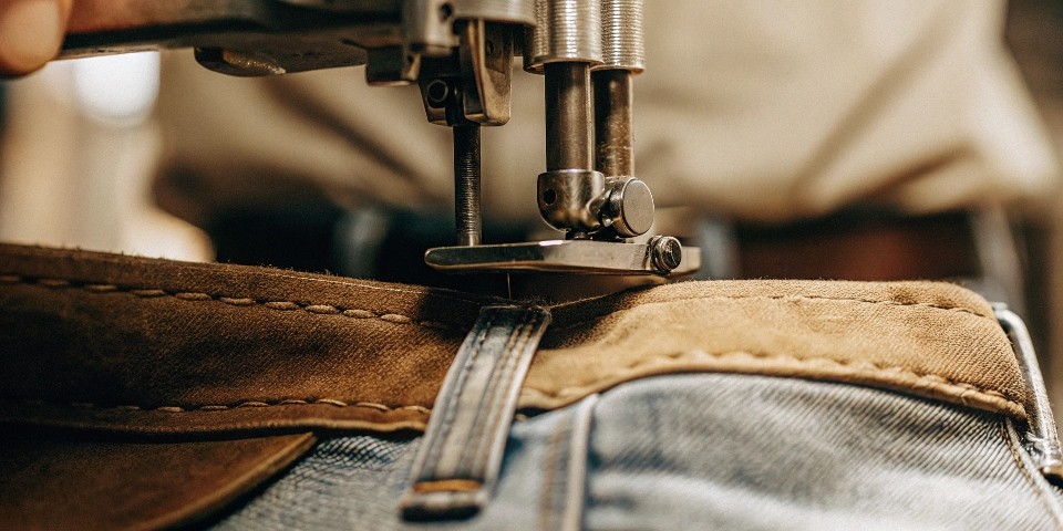 [A close-up shot of a branding machine pressing a custom leather patch onto the waistband of a pair of jeans.