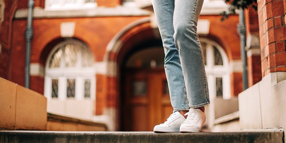A stylish person wearing straight-leg jeans that are intentionally long, showing the fabric "stacking" over their sneakers.