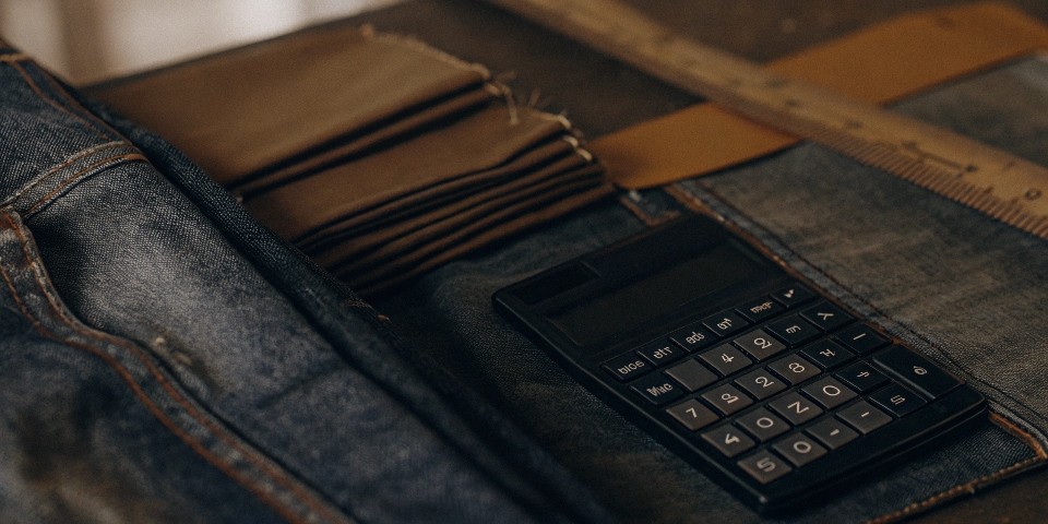 A calculator and a pile of denim fabric swatches, representing the costs of starting a jeans company.