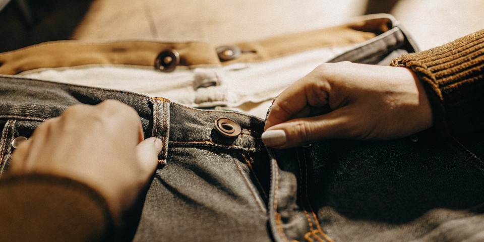 A close-up shot of a person's hands pointing out the specific stitching and hardware details on a pair of jeans.
