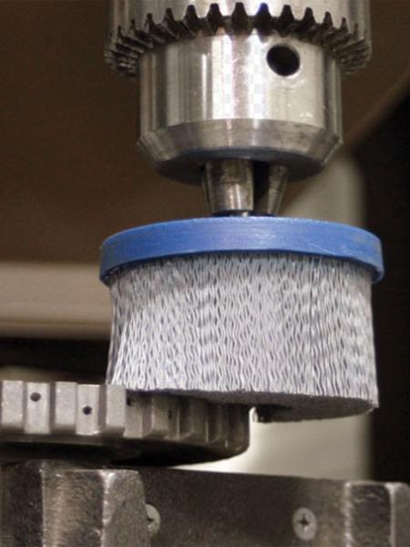 An industrial robot arm using a large abrasive filament wheel brush to deburr the edges of a complex aluminum automotive part.