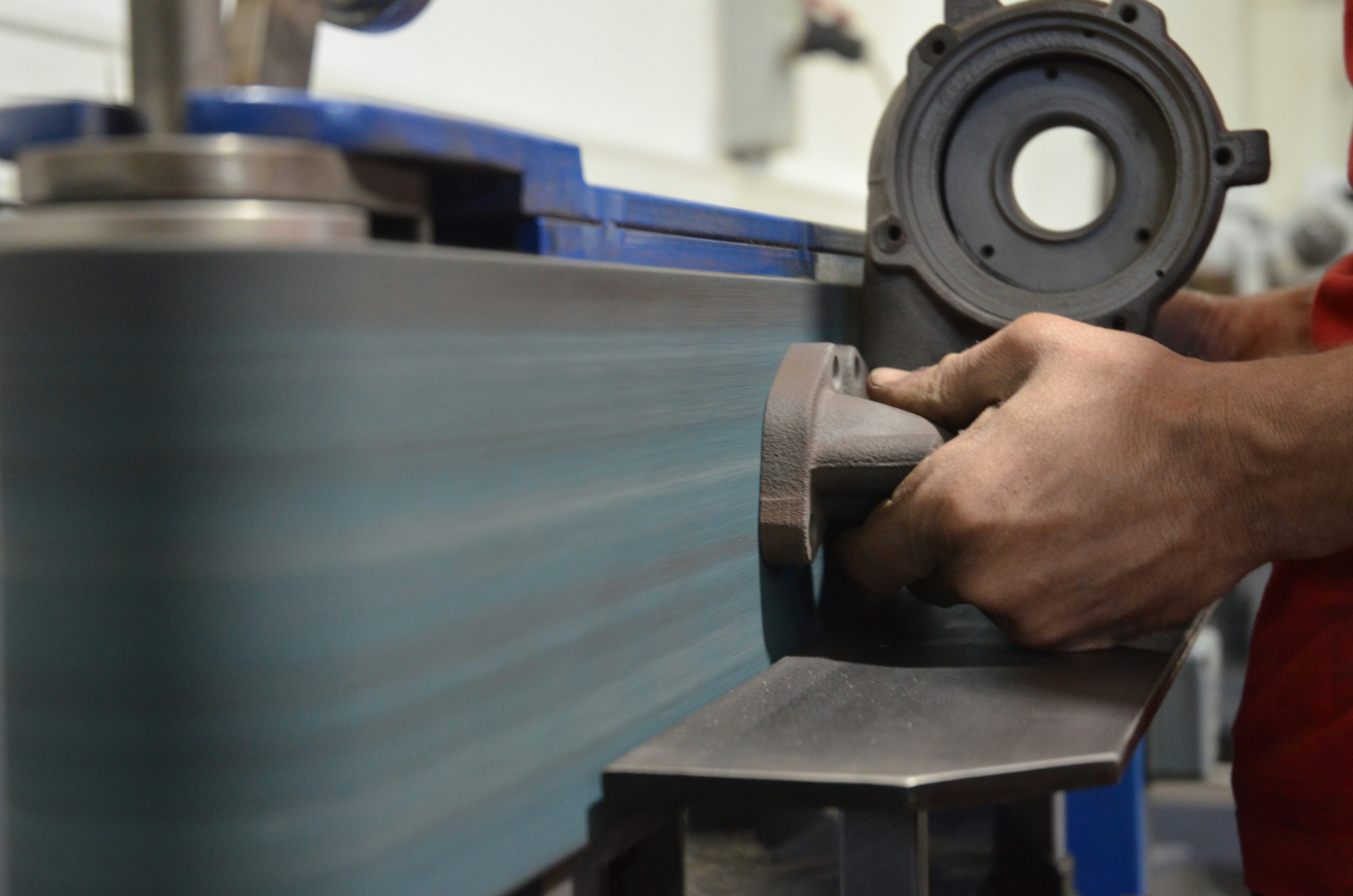 An industrial robot arm using a large abrasive filament wheel brush to deburr the edges of a complex aluminum automotive part.