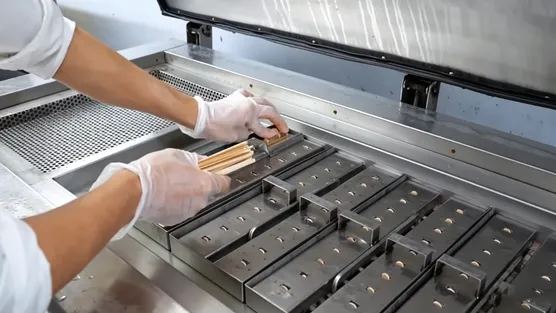 Manos insertando un palo de madera en un molde de helado recién relleno en un taller de lotes pequeños
