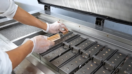 Hands inserting a wooden stick into a freshly filled ice cream mould in a small-batch workshop