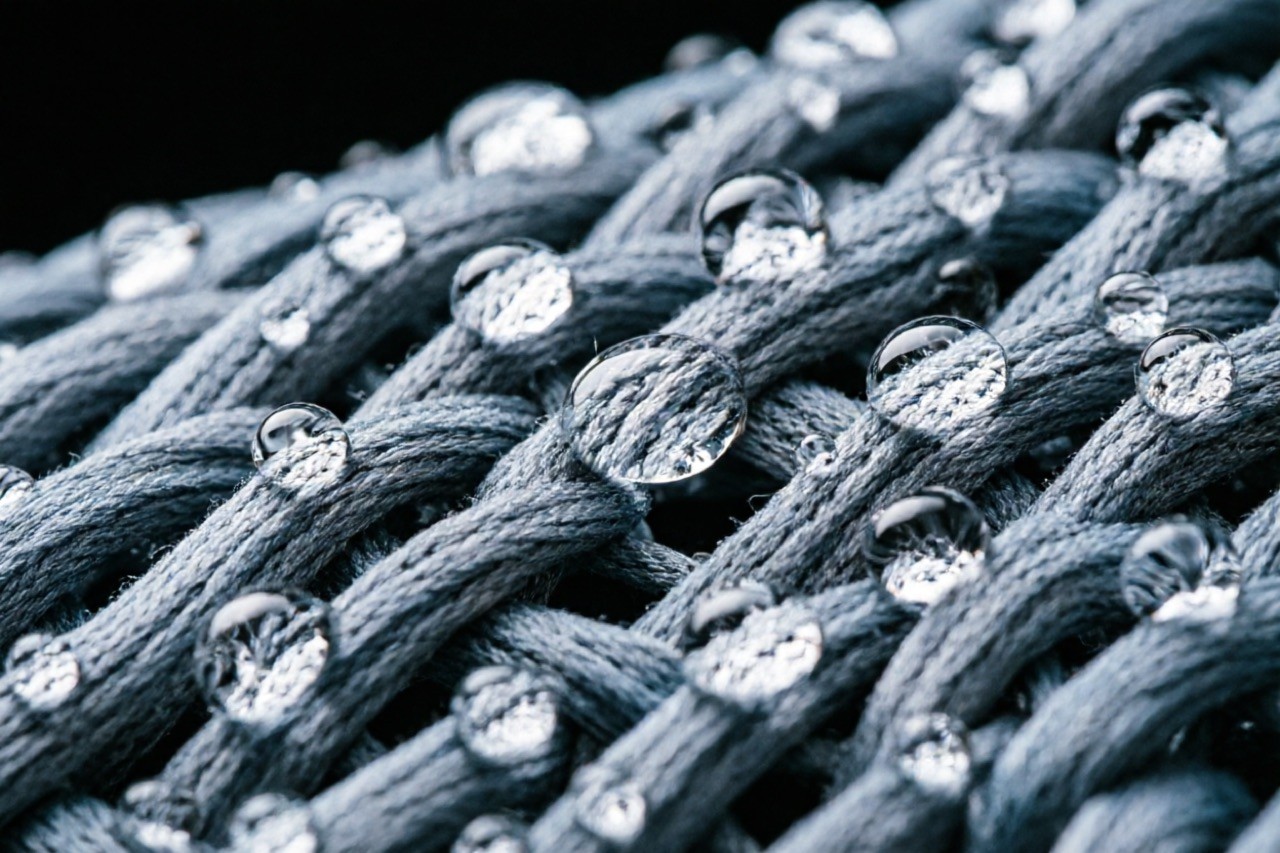 Dri-fit tank top fabric macro — micro-porous moisture-wicking knit structure with water droplets beading, technical sportswear material