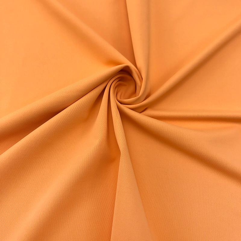 Twisted close-up of solid warm orange stretch knit fabric, Faybric AIR-ICY soft elastic cool touch sportswear textile