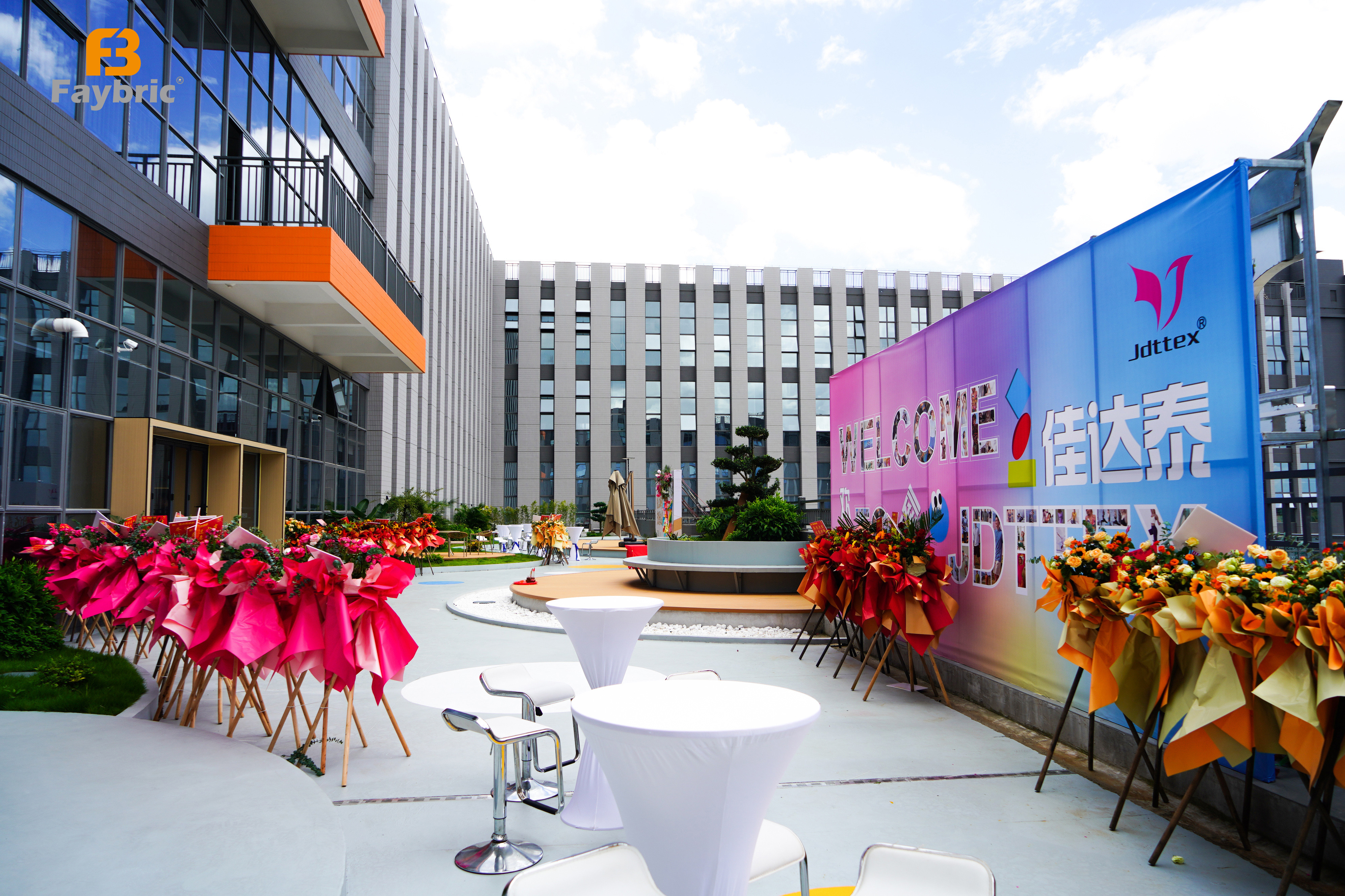 Outdoor festively decorated venue of Faybric Jdttex relocation with welcome backdrop and flower bouquets